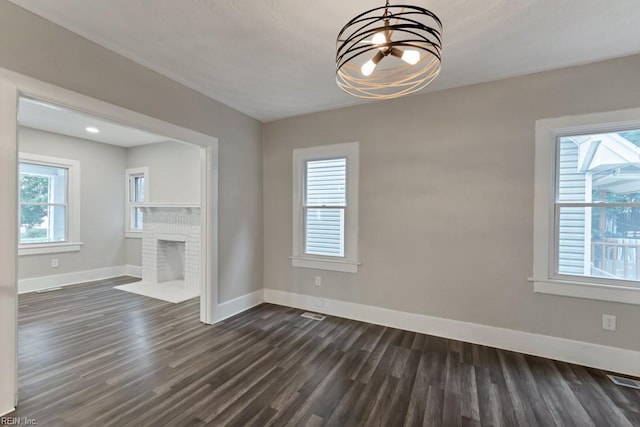 interior space with a brick fireplace, an inviting chandelier, and dark wood-type flooring