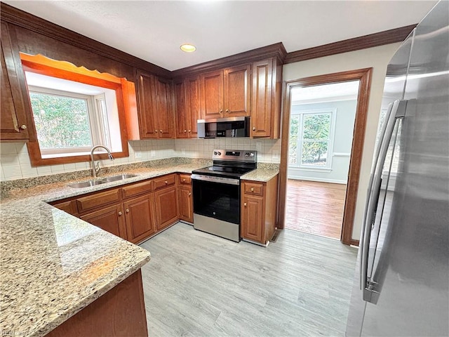 kitchen with crown molding, sink, light stone countertops, appliances with stainless steel finishes, and light hardwood / wood-style floors