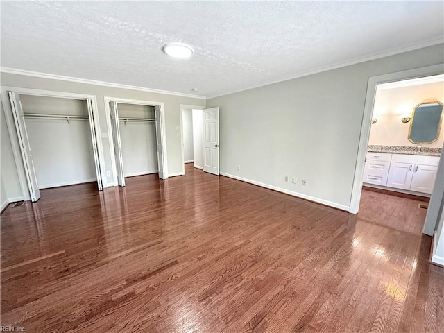 unfurnished bedroom featuring two closets, crown molding, ensuite bath, dark hardwood / wood-style floors, and a textured ceiling