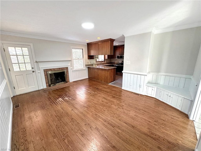 unfurnished living room featuring crown molding, sink, hardwood / wood-style floors, and a brick fireplace