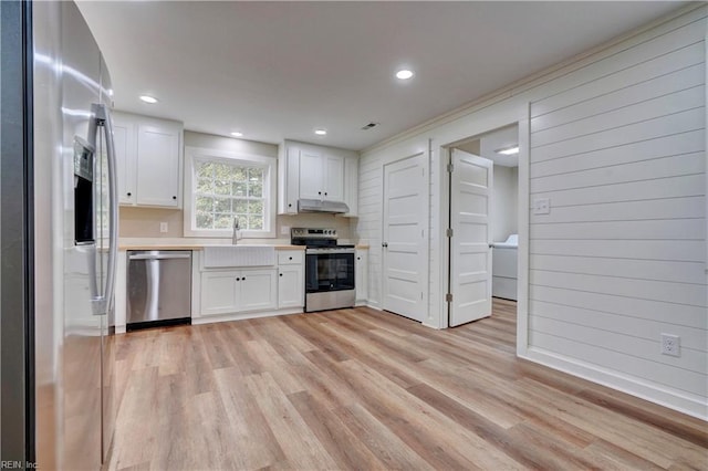 kitchen with appliances with stainless steel finishes, light wood-type flooring, sink, white cabinetry, and wood walls