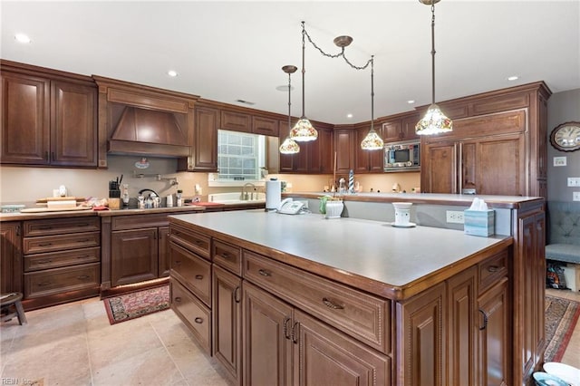 kitchen with stainless steel microwave, sink, hanging light fixtures, a kitchen island, and custom range hood