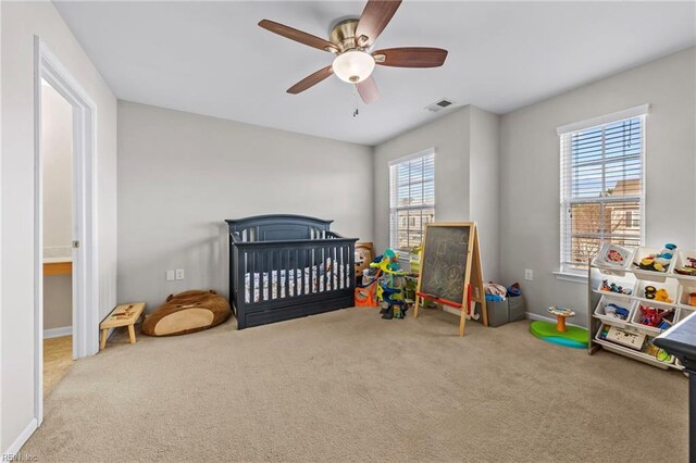 carpeted bedroom featuring ceiling fan and a nursery area