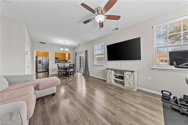 living room with vaulted ceiling, light hardwood / wood-style flooring, and ceiling fan with notable chandelier