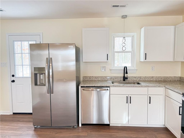 kitchen with light stone countertops, appliances with stainless steel finishes, sink, decorative light fixtures, and white cabinetry