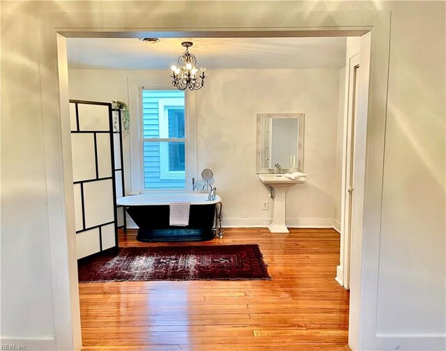 interior space with a chandelier, a bathtub, and hardwood / wood-style floors