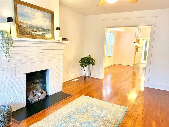 unfurnished living room featuring a brick fireplace, wood-type flooring, ceiling fan, and baseboards