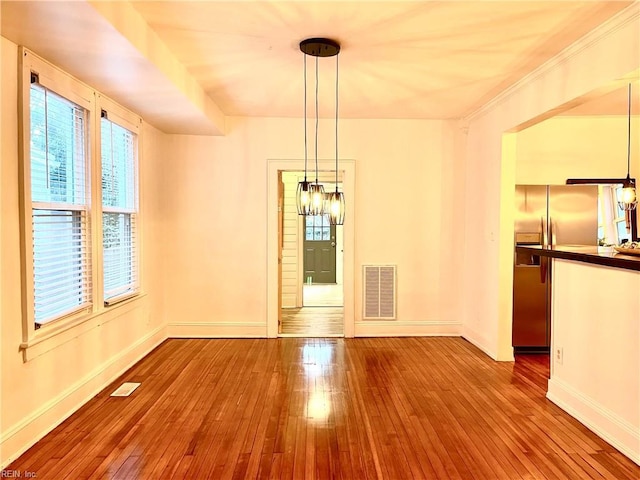 unfurnished dining area featuring crown molding, a chandelier, and hardwood / wood-style flooring