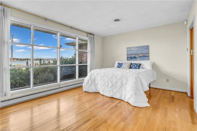 bedroom with a baseboard heating unit, a water view, and light hardwood / wood-style flooring