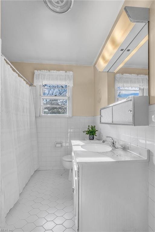 bathroom featuring toilet, tile patterned floors, vanity, and tile walls