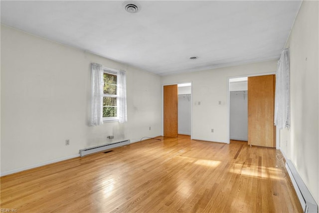 unfurnished bedroom with light hardwood / wood-style floors, baseboard heating, and a spacious closet