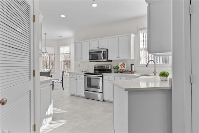 kitchen featuring sink, kitchen peninsula, appliances with stainless steel finishes, decorative light fixtures, and white cabinetry