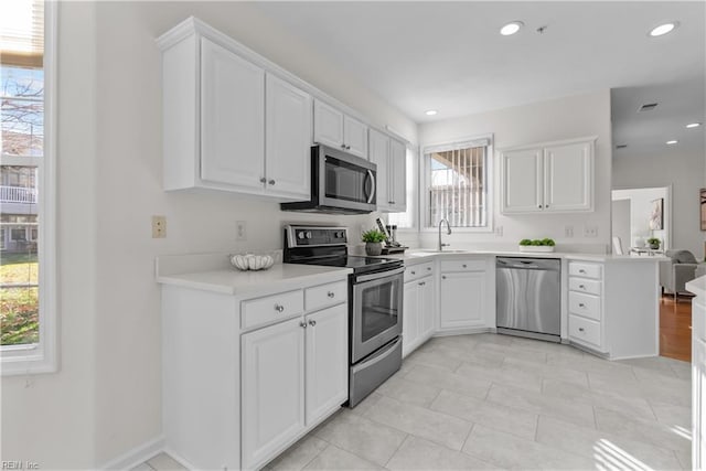 kitchen with white cabinets, sink, light tile patterned floors, kitchen peninsula, and stainless steel appliances