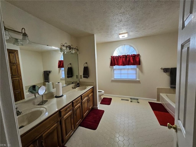 bathroom featuring a bathing tub, vanity, a textured ceiling, and toilet