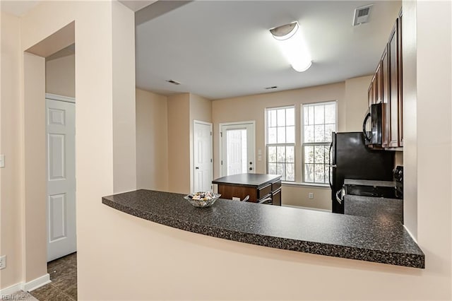 kitchen with kitchen peninsula, black appliances, and dark tile patterned flooring