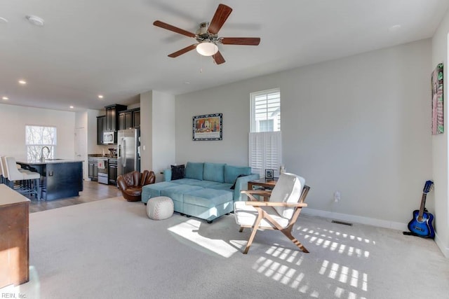 carpeted living room featuring ceiling fan and sink