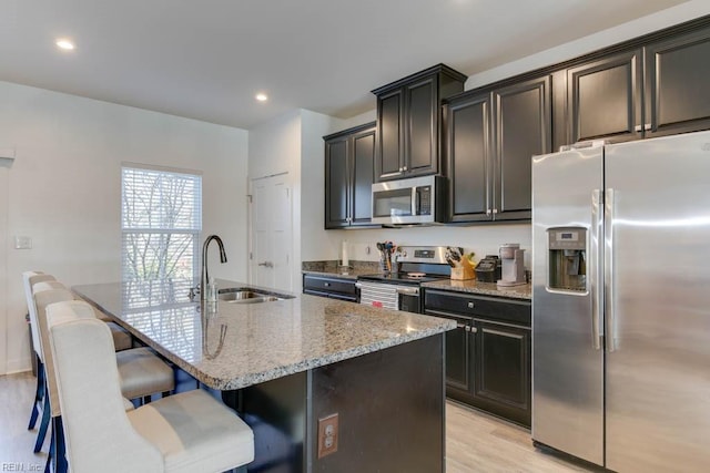 kitchen with stainless steel appliances, sink, a center island with sink, light hardwood / wood-style flooring, and a breakfast bar area