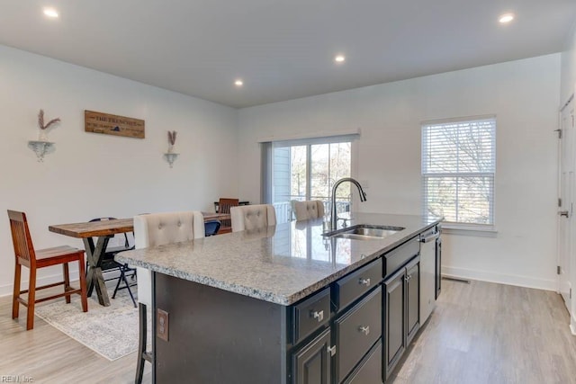 kitchen with a center island with sink, light stone countertops, light wood-type flooring, and sink