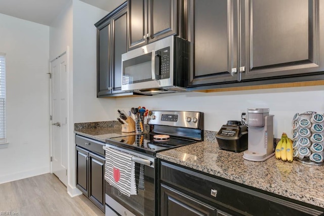 kitchen with appliances with stainless steel finishes, light hardwood / wood-style flooring, and light stone counters