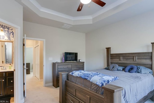 bedroom with a raised ceiling, connected bathroom, ceiling fan, and light colored carpet