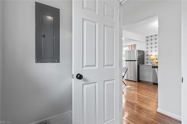 corridor featuring electric panel, light hardwood / wood-style floors, and a textured ceiling