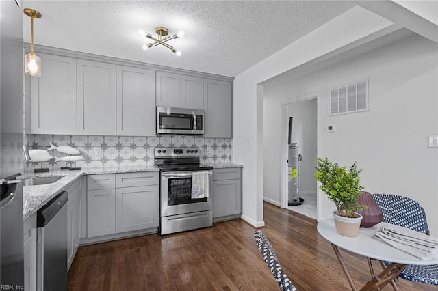 kitchen featuring gray cabinetry, light stone counters, decorative light fixtures, decorative backsplash, and appliances with stainless steel finishes