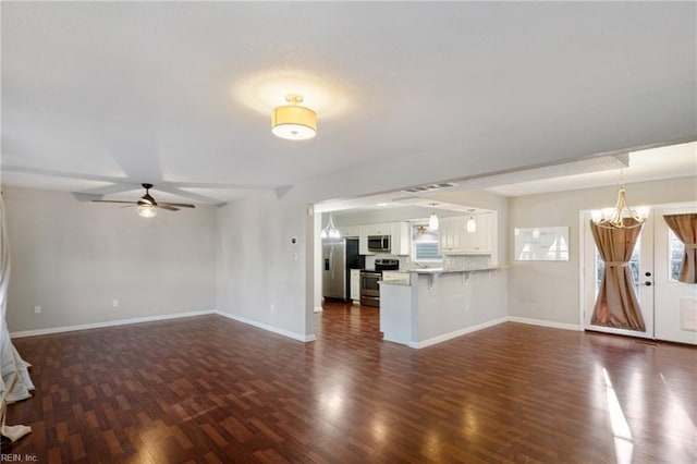 unfurnished living room featuring dark wood-type flooring and ceiling fan with notable chandelier