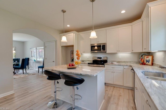 kitchen with stainless steel appliances, sink, white cabinetry, light stone counters, and light hardwood / wood-style floors