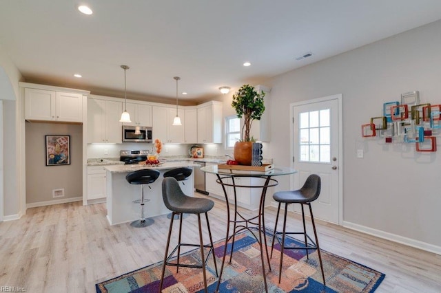 kitchen featuring stainless steel appliances, white cabinetry, pendant lighting, a kitchen island, and a breakfast bar