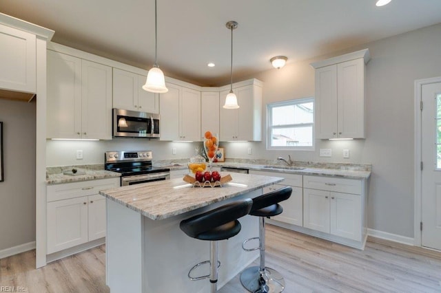 kitchen featuring white cabinetry, light stone counters, light wood-type flooring, hanging light fixtures, and appliances with stainless steel finishes