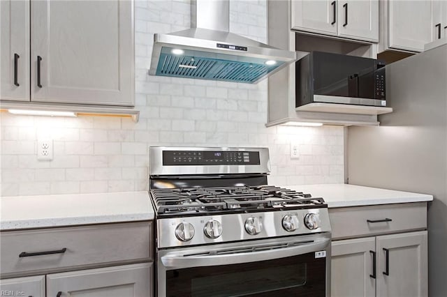 kitchen featuring stainless steel appliances, light stone countertops, backsplash, gray cabinets, and wall chimney range hood