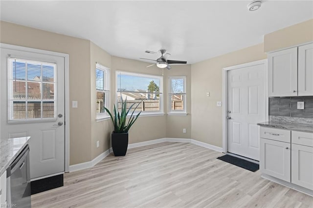 interior space featuring ceiling fan, stainless steel dishwasher, decorative backsplash, white cabinetry, and light stone counters