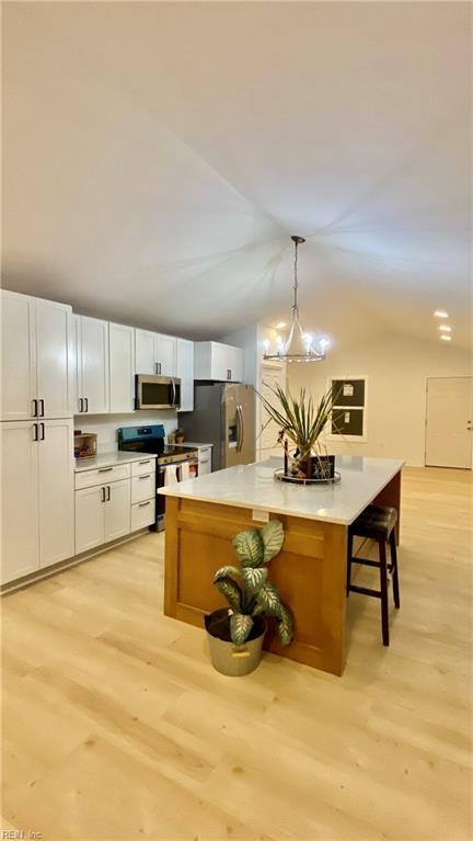 kitchen featuring light wood finished floors, a kitchen island, stainless steel appliances, light countertops, and lofted ceiling