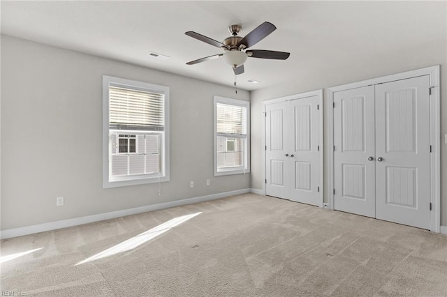 unfurnished bedroom featuring ceiling fan, light carpet, and multiple closets