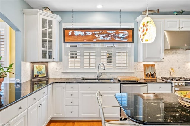 kitchen featuring sink, white cabinets, wall chimney exhaust hood, dark stone countertops, and hanging light fixtures