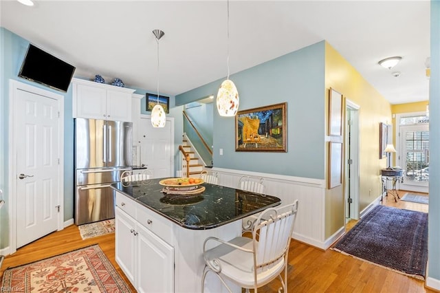 kitchen with white cabinets, light hardwood / wood-style flooring, stainless steel refrigerator, dark stone counters, and a kitchen island