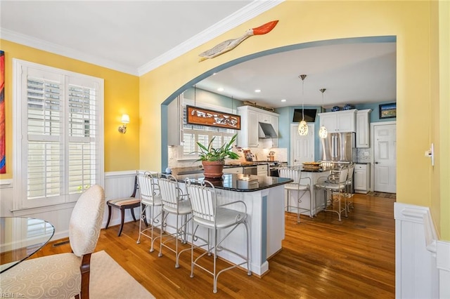 kitchen with kitchen peninsula, dark wood-type flooring, a kitchen bar, white cabinetry, and decorative light fixtures