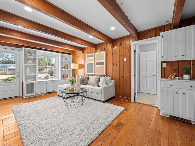 living room featuring light hardwood / wood-style floors, beamed ceiling, and wooden walls