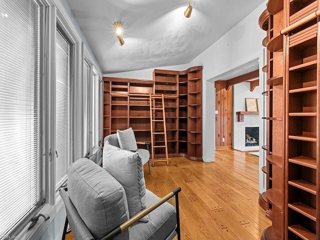 living area featuring wood-type flooring, a brick fireplace, and vaulted ceiling