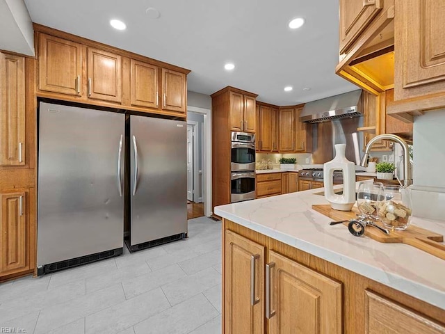 kitchen with stainless steel appliances, wall chimney range hood, and light stone countertops