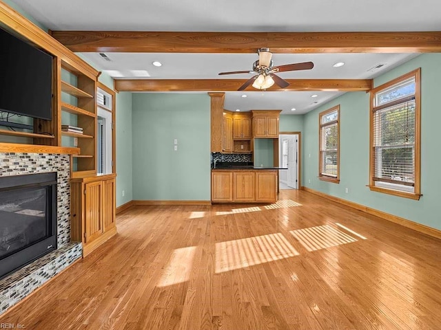 unfurnished living room featuring light wood-type flooring, a tiled fireplace, and beamed ceiling