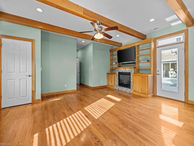 unfurnished living room featuring ceiling fan, light hardwood / wood-style flooring, a tiled fireplace, and beamed ceiling