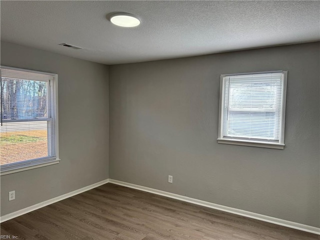 spare room featuring a textured ceiling, dark hardwood / wood-style floors, and a wealth of natural light