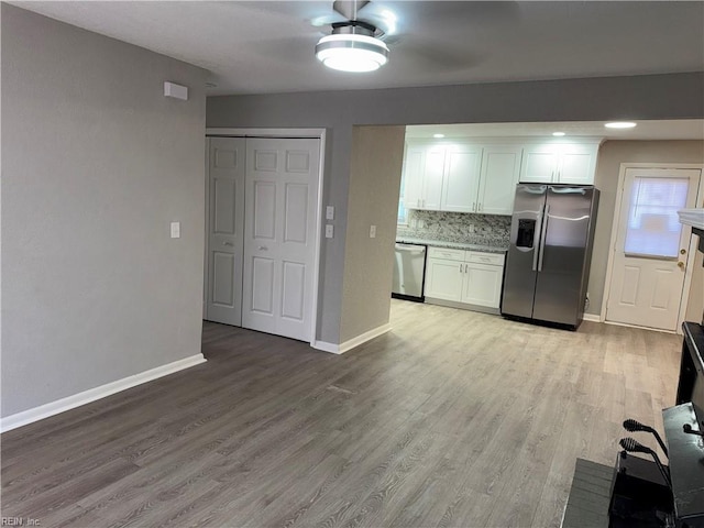 kitchen with light stone countertops, stainless steel appliances, tasteful backsplash, white cabinets, and light wood-type flooring