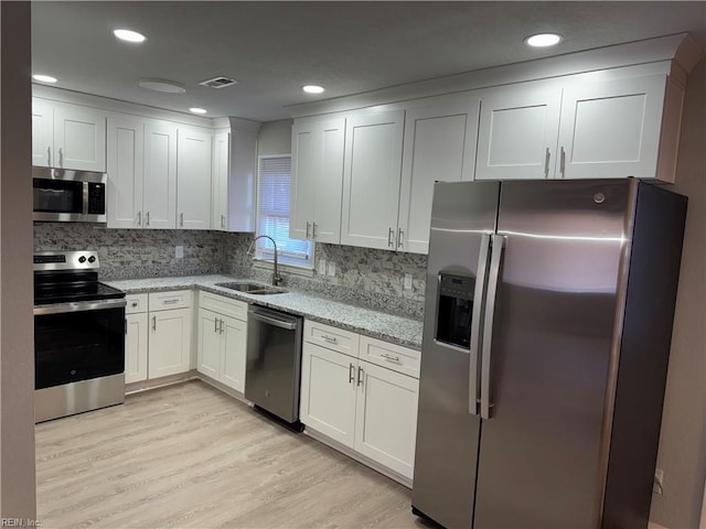 kitchen with light stone counters, stainless steel appliances, white cabinetry, and sink