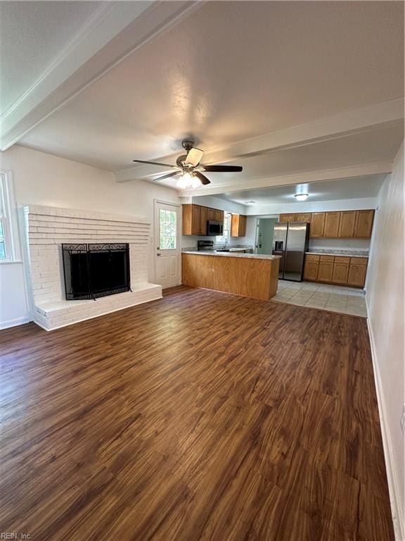 unfurnished living room with ceiling fan, beam ceiling, light hardwood / wood-style flooring, and a brick fireplace