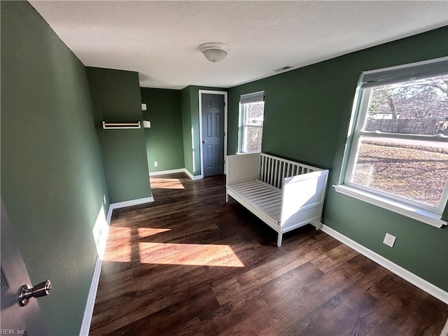 unfurnished bedroom with multiple windows, dark hardwood / wood-style flooring, and a crib