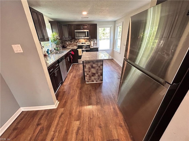 kitchen with backsplash, dark brown cabinetry, stainless steel appliances, sink, and a center island