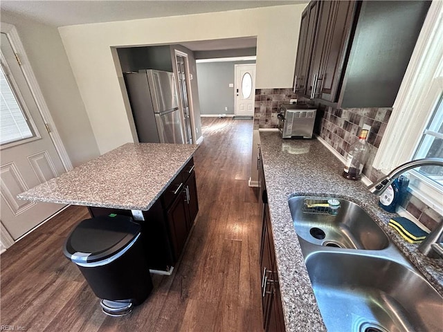 kitchen with sink, decorative backsplash, stainless steel fridge, a kitchen island, and dark brown cabinetry