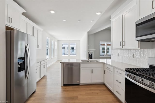 kitchen with white cabinetry, sink, kitchen peninsula, appliances with stainless steel finishes, and light wood-type flooring